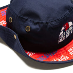 Rex Club | A close-up of a navy bucket hat with a red interior and brass eyelets. the hat features a cartoon-style embroidered patch and printed text around the brim. | Custom Caps | Custom Hats | Team Headwear | UK
