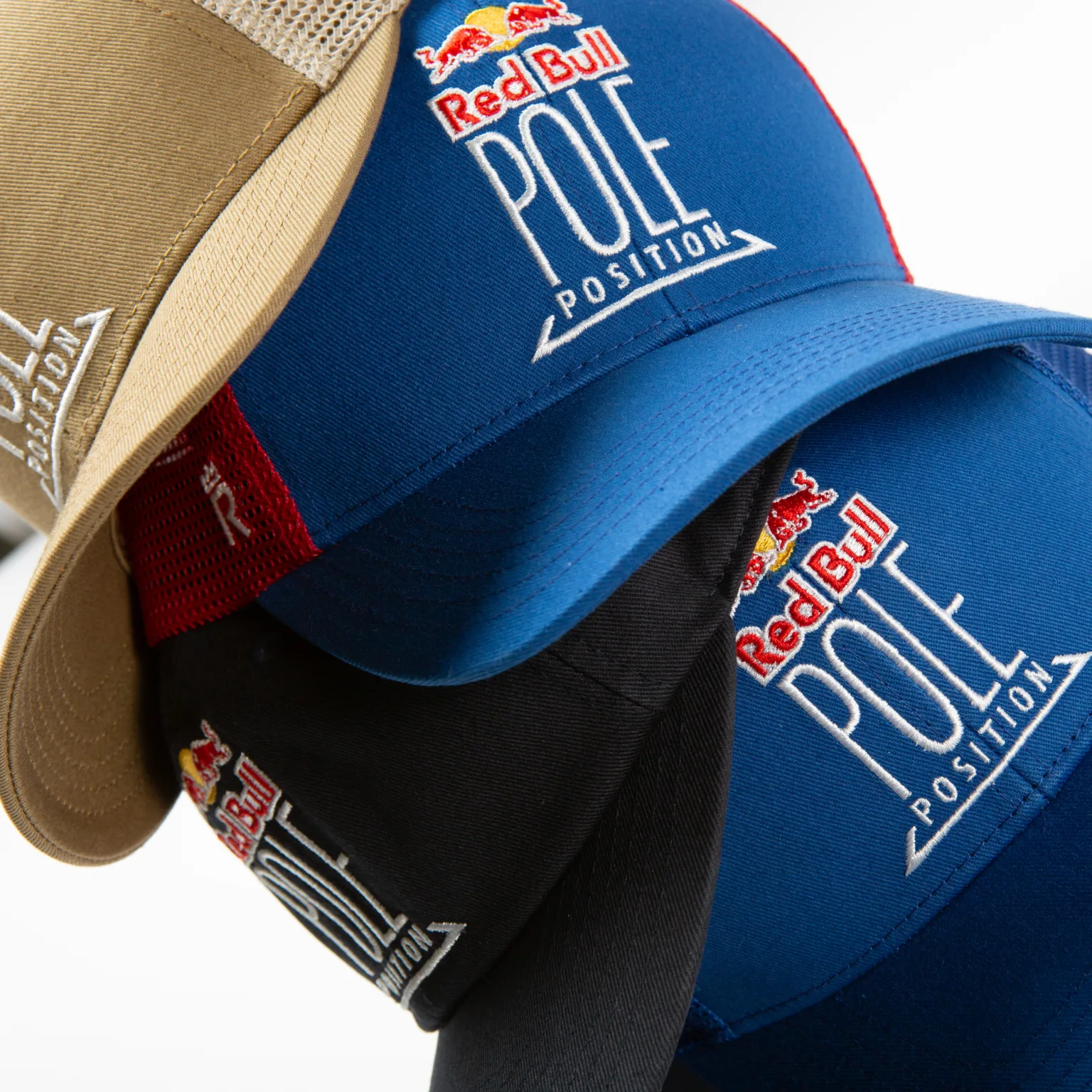 Rex Club | Three caps stacked on top of each other, each embroidered with the Red Bull logo and the words "Pole Position." The caps are blue, black, and beige, with mesh backs and angled brims. | Custom Caps | Custom Hats | Team Headwear | UK