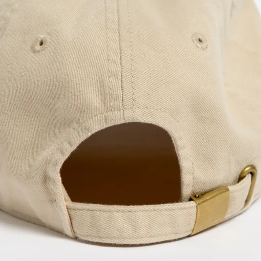 Rex Club | Close-up of the back of a beige baseball cap showing an adjustable strap with a brass-colored metal buckle and eyelets for ventilation. | Custom Caps | Custom Hats | Team Headwear | UK