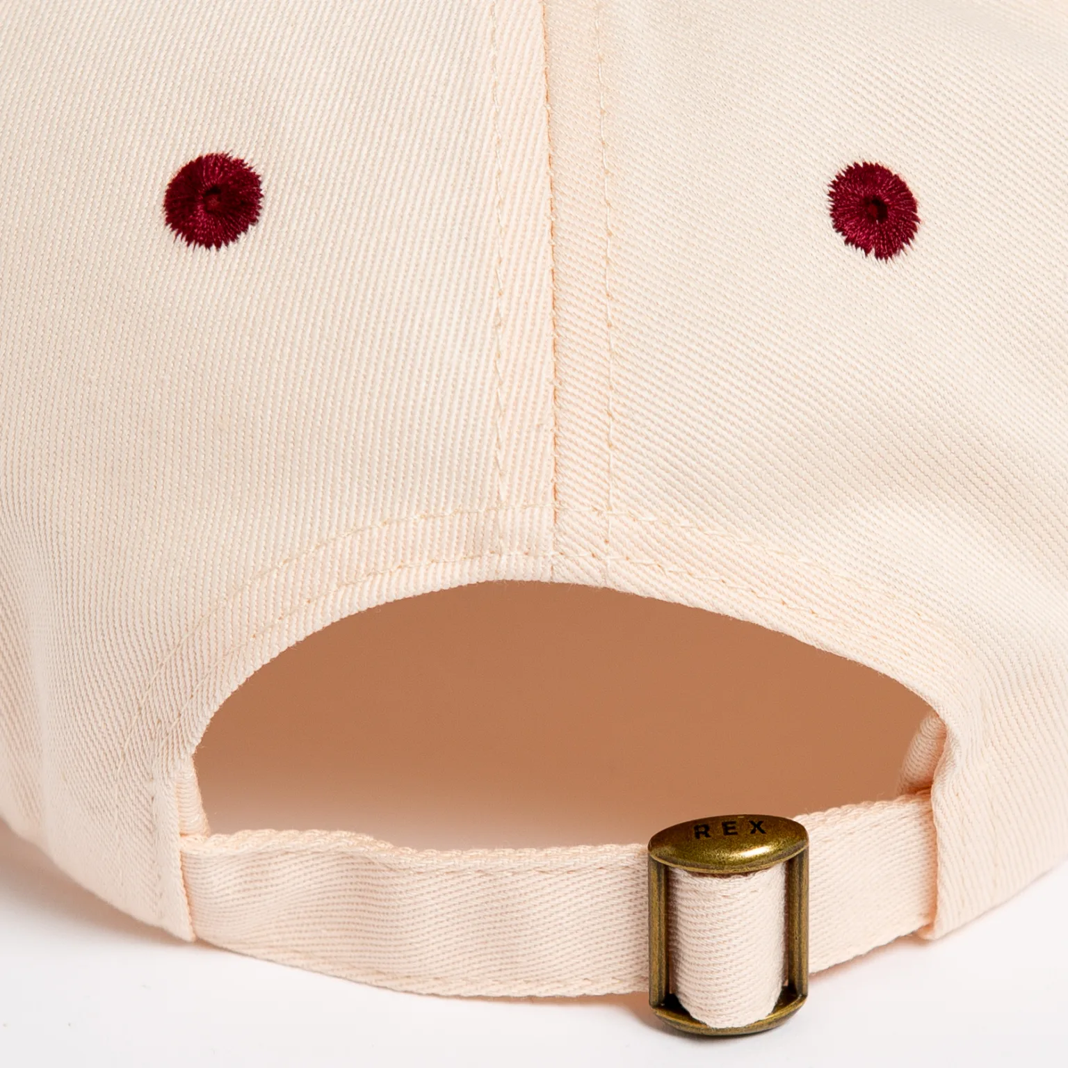 Rex Club | Close-up of the back of the Rex Club - TwoTone - Canvas Cap in light beige, featuring red stitched eyelets and an adjustable strap with a gold buckle engraved with "REX. | Custom Caps | Custom Hats | Team Headwear | UK