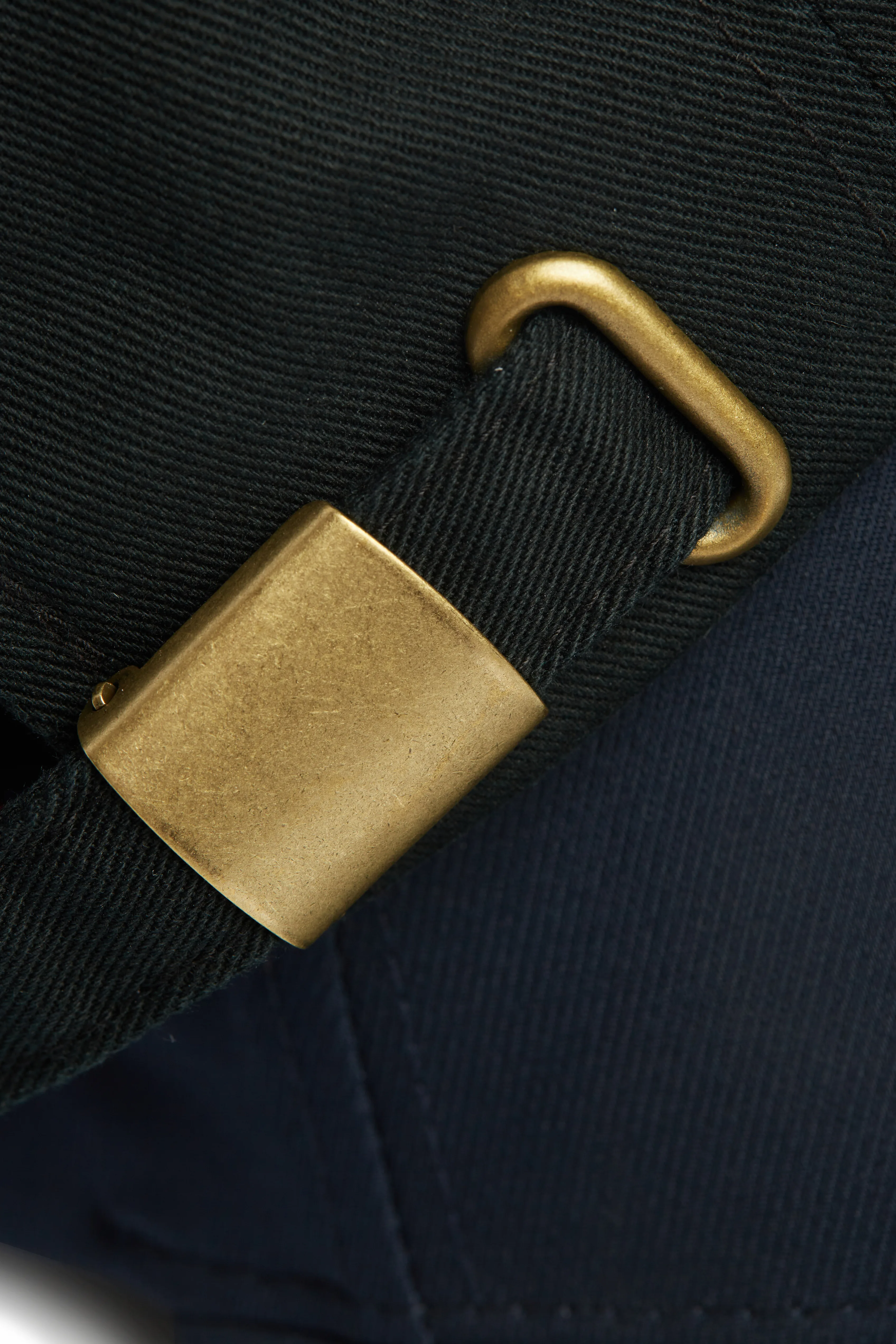 Rex Club | Norway Rugby Slouch | Custom Caps | Custom Hats | Team Headwear | UK Rex Club | Close-up of the Norway Rugby Stretch's brass buckle and clasp on a dark fabric strap, highlighting the detailed texture of both the material and shiny metal hardware. | Custom Caps | Custom Hats | Team Headwear | UK