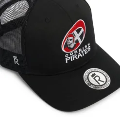 Rex Club | The Cornish Pirates - Club Crest Trucker is a black cap with the Pirates logo featuring a pirate face and crossed swords on the front, a round sticker on the brim, and mesh material at the back. | Custom Caps | Custom Hats | Team Headwear | UK
