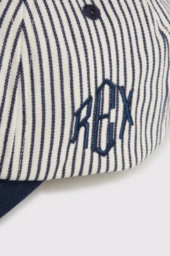 Rex Club | A close-up of the RC - Baseball Pin - SS26 Navy cap: white with thin navy blue vertical stripes, 