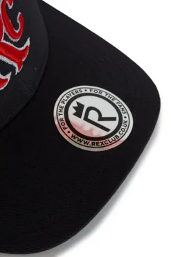 Close-up of a black baseball cap featuring a circular sticker on the brim with red embroidery nearby