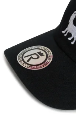 Rex Club | A close-up of the brim of the Goat black cap featuring a circular sticker with “FOR THE PLAYERS, FOR THE FANS” and a crown with an 