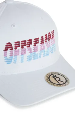 White baseball cap with a multicolor embroidered pattern along the brim and a circular sticker on the front edge of the brim.