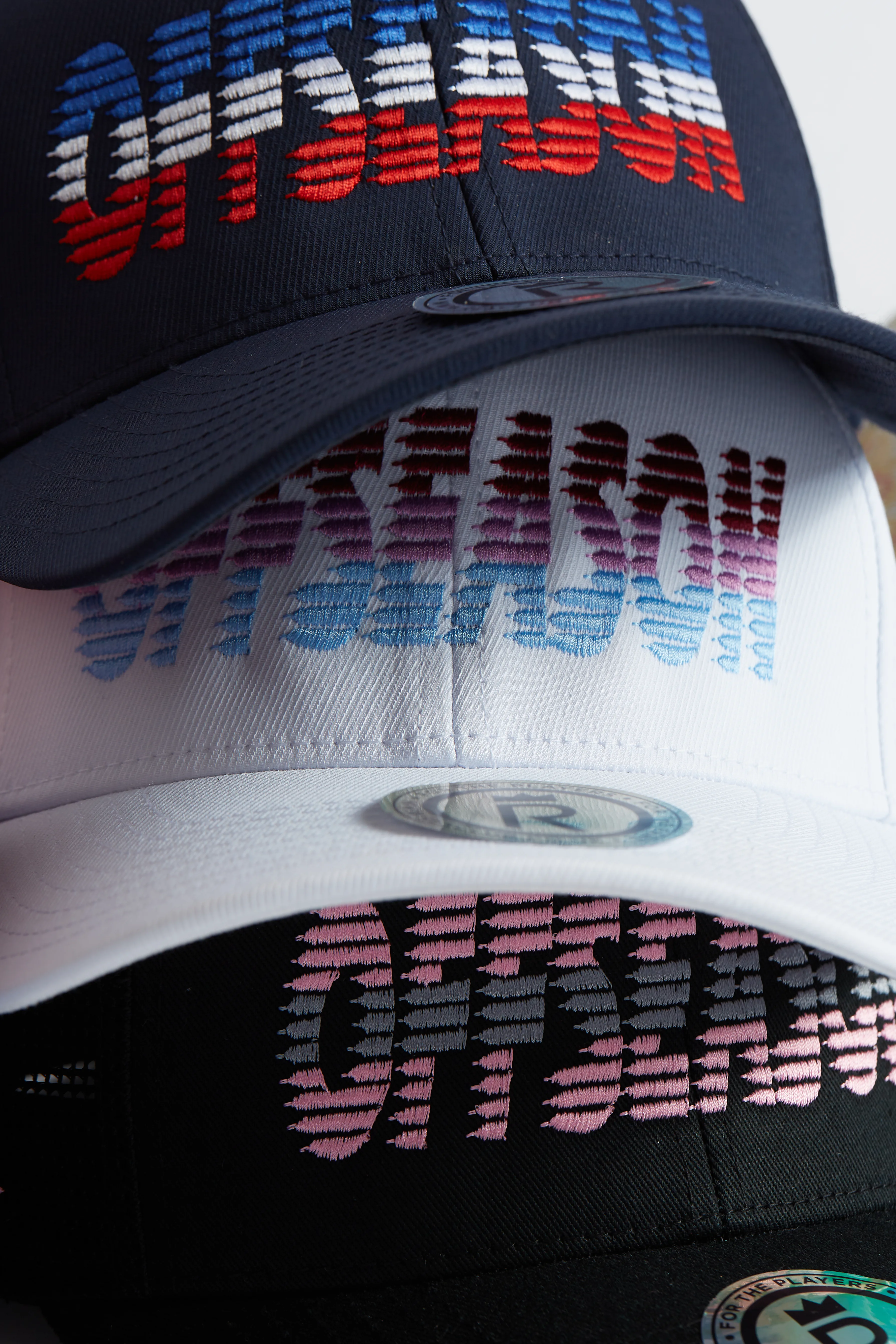 Rex Club | Three baseball caps stacked on top of each other display the word "OFFSEASON" in colourful, horizontal gradient lettering: blue and red on navy, purple and teal on white, and pink and purple on black. | Custom Caps | Custom Hats | Team Headwear | UK